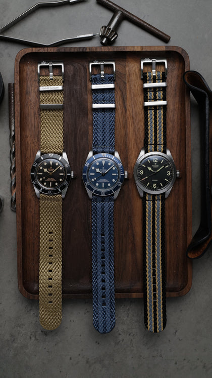 Luxurious Apex two-piece watch straps displayed with elegant watches on a wooden tray, complemented by watchmaking tools on a grey surface - Under the Cuff's Apex Collection epitomising style and precision